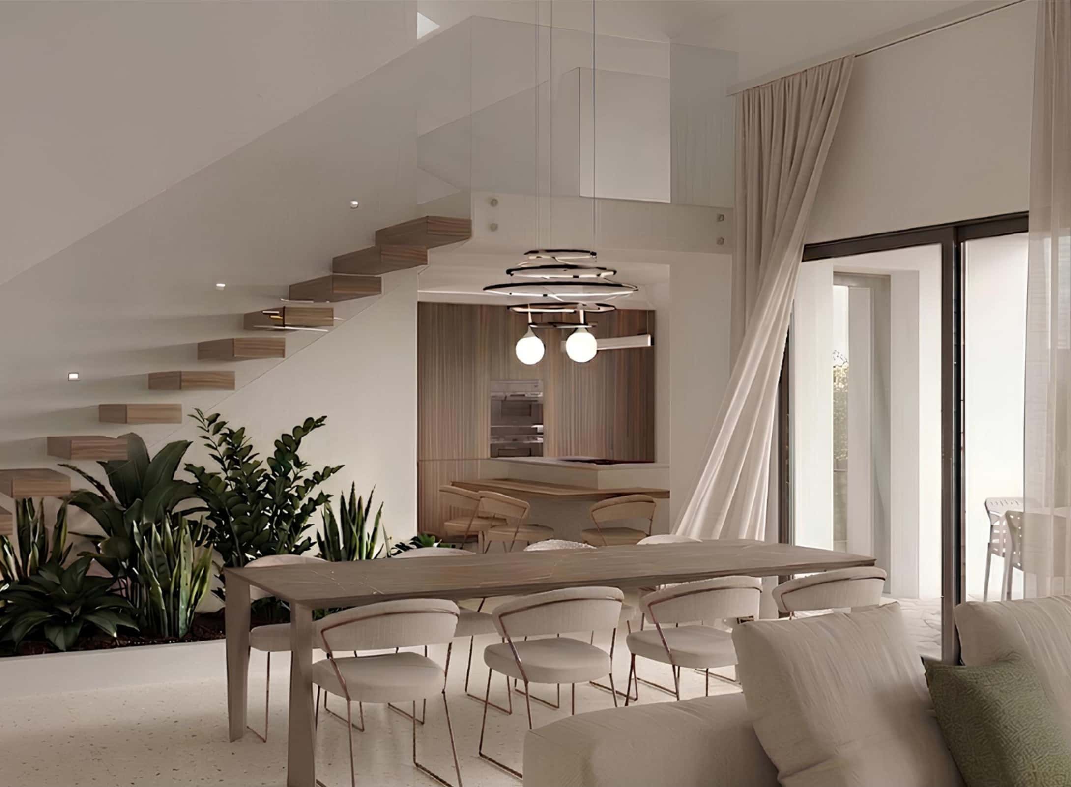 Modern interior with floating stairs, large dining table, white chairs, lush plants underneath stairs, pendant lights, and sheer curtains by a window.