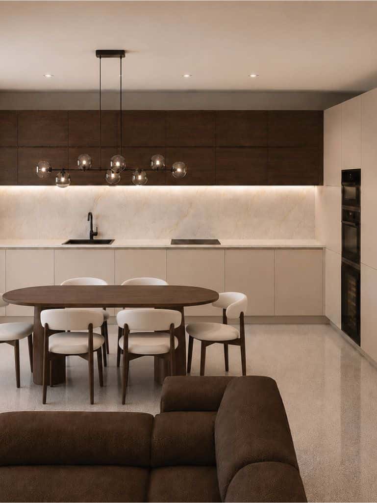 Cucina lineare con pensili in legno scuro, tavolo da pranzo ovale in legno e ampie vetrate affacciate sul giardino.